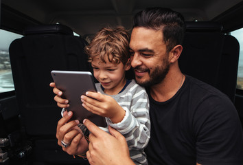 Happy father and son on road trip using digital tablet