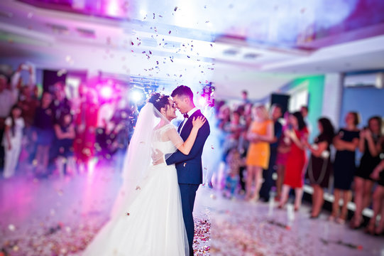 Touching and emotional first dance of the couple on their wedding with confetti and colorful lights on the background.