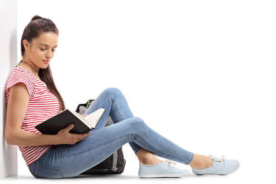Teenage student leaning against a wall and reading a book