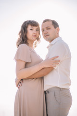 Fototapeta premium beautiful couple, the girl in the beige dress, the man in white shirt standing close to each other against the white blue sky, sun, close-up, summer, heat, nature, love story