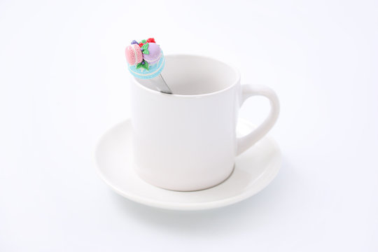 White cup and a plate with a spoon, a cake and pink roses on a white background