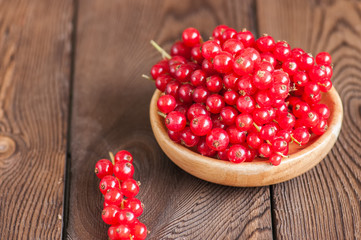 Close up of heap of red currants in a wooden plate. Wooden background. Copy space. Selective focus.