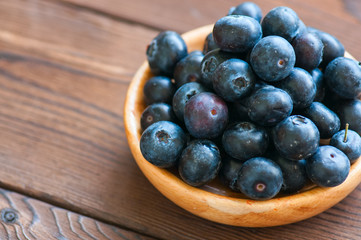 Heap of fresh raw blueberries in a wooden plate. Wooden background. Copy space and close up.