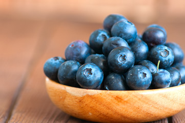 Heap of fresh raw blueberries in a wooden plate. Wooden background. Copy space and close up.