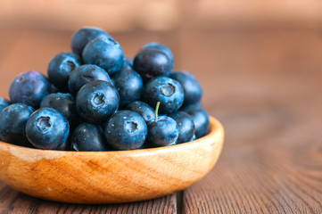 Heap of fresh raw blueberries in a wooden plate. Wooden background. Copy space and close up.