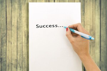 Woman's hand writing word success on white paper sheet, wooden background