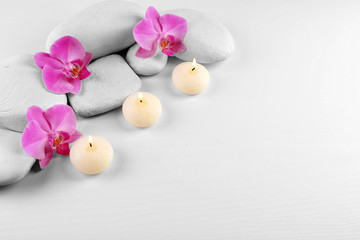 Fototapeta na wymiar Spa stones with orchid flowers and burning candles on white background