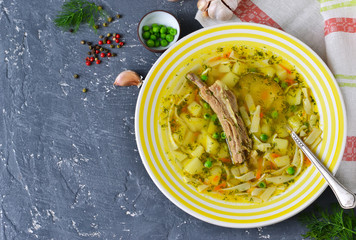Homemade soup with ribs, noodles and green peas on a concrete background.