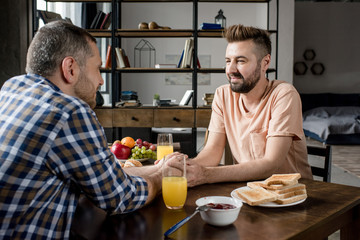 Fototapeta na wymiar Homosexual couple holding hands and looking at each other during breakfast