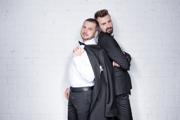young couple of grooms in suits posing and looking at camera indoors