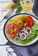 Vegetable mix salad with avocado and olive oil sauce on a white, wooden background.