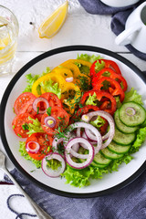 Vegetable mix salad with avocado and olive oil sauce on a white, wooden background.