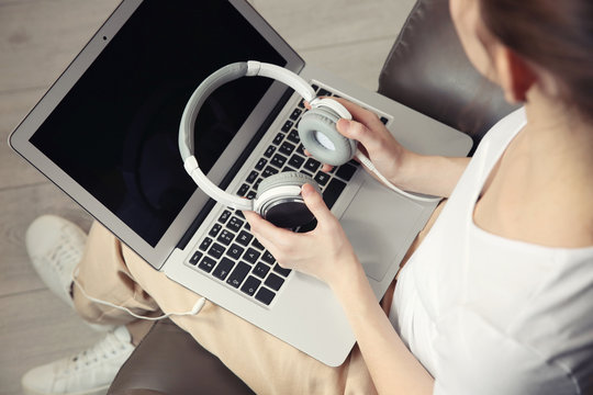 Audio book concept. Young woman using laptop with headphones, close up