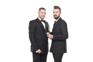 homosexual couple of grooms in suits posing and looking at camera isolated on white