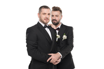 couple of grooms in suits embracing and looking at camera isolated on white