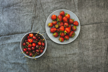 Bowl of fresh strawberries and cherries on a background of gray linen