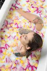 Obraz na płótnie Canvas Delightful girl with wet hair and colorful tattoos sits in the w