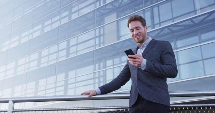 Phone. Business man using phone sms texting using app on smartphone in city business district. Young businessman using mobile phone smiling happy in suit jacket outdoors. Urban male professional