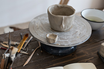 Close up of still life fresh clay pot for flowers or accessories, carefully and lovingly carved out of fresh mud material, artisan hand made piece with tools and brushes around