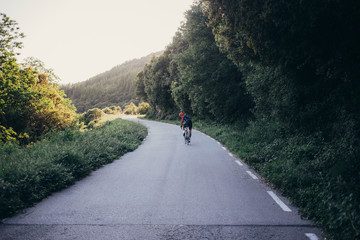 Athletic fit healthy young man rides professional carbon bicycle on quiet and empty mountain road,...