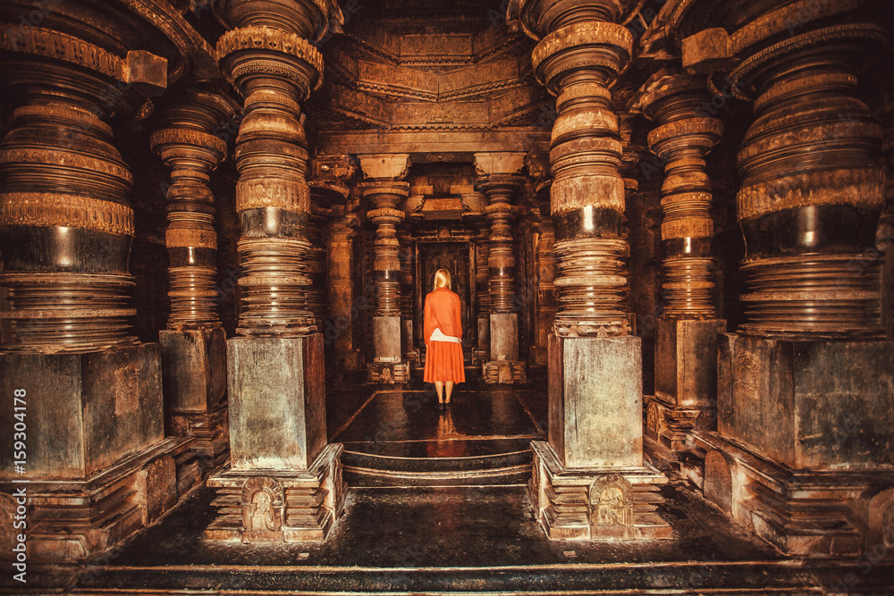 Wall mural Lonely woman standing in center of ancient Hindu temple with stone columns, India. Traditional architecture of Asia.