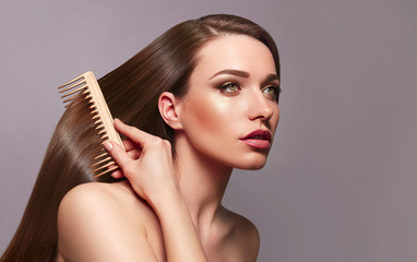 A beautiful young girl with long shiny silky hair sits and combs her hair with a golden comb. Cosmetics for hair, care, spa, beauty, fashion. Beauty saloon. Smooth skin. Advertising. Radiance, shine.