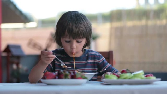 Cute child, preschool boy, eating spaghetti for lunch outdoors in garden