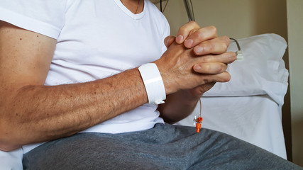 Male patient praying seated on a hospital bed