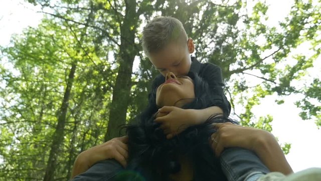 Young beautiful mom carrying her happy son on her shoulders with trees in background