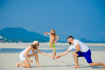 Happy young family of three having fun on the desert sunny beach