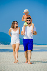 Happy young family of three having fun on the desert sunny beach