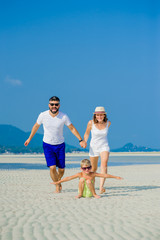 Happy young family of three having fun on the desert sunny beach