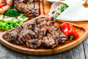 Assorted delicious grilled meat and vegetables with fresh salad and bbq sauce on cutting board on...