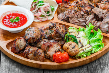 Assorted delicious grilled meat and vegetables with fresh salad and bbq sauce on cutting board on wooden background close up. Hot Meat Dishes. Top view
