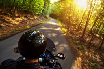Close-up of motorbiker riding on empty road in forest with sunset light, concept of speed and touring in nature.