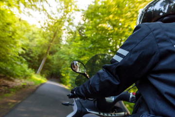 Close-up of motorbiker riding on empty road in forest with sunset light, concept of speed and touring in nature.