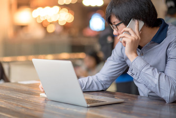 Young Asian Business man dressed in casual style contact with customer when working in cafe. Digital nomad lifestyle in public working space.