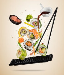 Flying sushi pieces served on plate, separated on colored background. Many kinds of popular sushi food with chopsticks. Concept of flying asian dish with ingredients