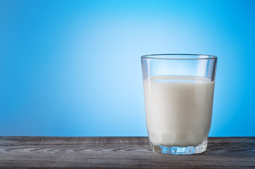 Glass of milk on wooden table with blue background
