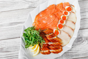 Seafood platter with salmon slice, smoke sturgeon, quail eggs with red caviar, slices fish fillet, decorated with arugula and lemon on wooden background close up. Mediterranean appetizers. Top view