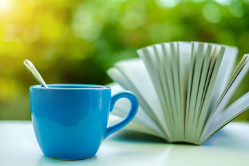 A blue cup of coffee with blurred opened book and green natural background