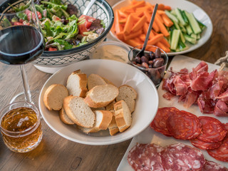 Wine appetizer set. Glass of red wine, baguette, olives, smoked meat, salad and salami on a rustic wooden table.