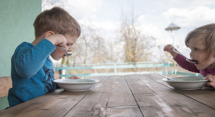 Little boy and girl eating soup with spoon in mouth