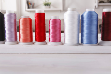 Colorful thread spools on wooden table close up