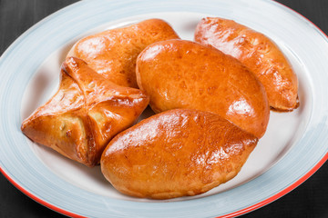 Fresh bread buns pies patties in plate on black wooden background. Bakery products. Hot and healthy breakfast, top view, flat lay