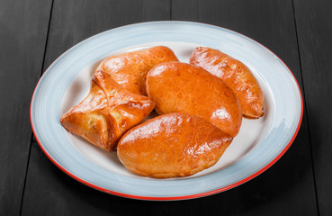 Fresh bread buns pies patties in plate on black wooden background. Bakery products. Hot and healthy breakfast, top view, flat lay