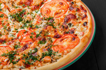 Pizza with chicken, tomatoes, mushrooms, greens and cheese on dark wooden background. Homemade pizza. Top view