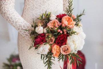 Closeup of young beauty skinny bride holding perfect bridal bouquet of fresh colorful flowers in hands. Happy woman wearing white gorgeous wedding dress. Color picture.