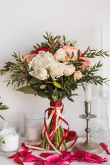 Closeup of beautiful bridal bouquet of fresh flowers of red, white, pink, pastel colors. Bunch decorated with many ribbons stands on table ready for ceremony. Vertical color photo.