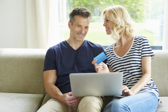 Spending money on the internet. Shot of a happy middle aged couple using laptop and credit card while sitting at home and shopping online. 